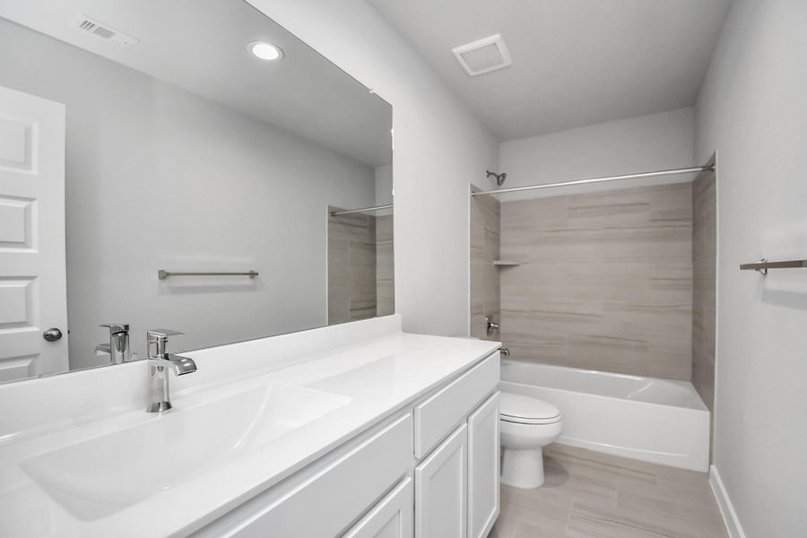 The secondary bath boasts stylish tile flooring, a bath/shower combo with a sleek tile surround, light wood cabinets, and a stunning light countertop. Sample photo of completed home with similar floor plan. Actual colors and selections may vary.