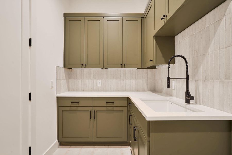 Kitchen with light countertops, tile walls, green cabinets, and tasteful backsplash Kitchen with light countertops, tile walls, green cabinets, and tasteful backsplash