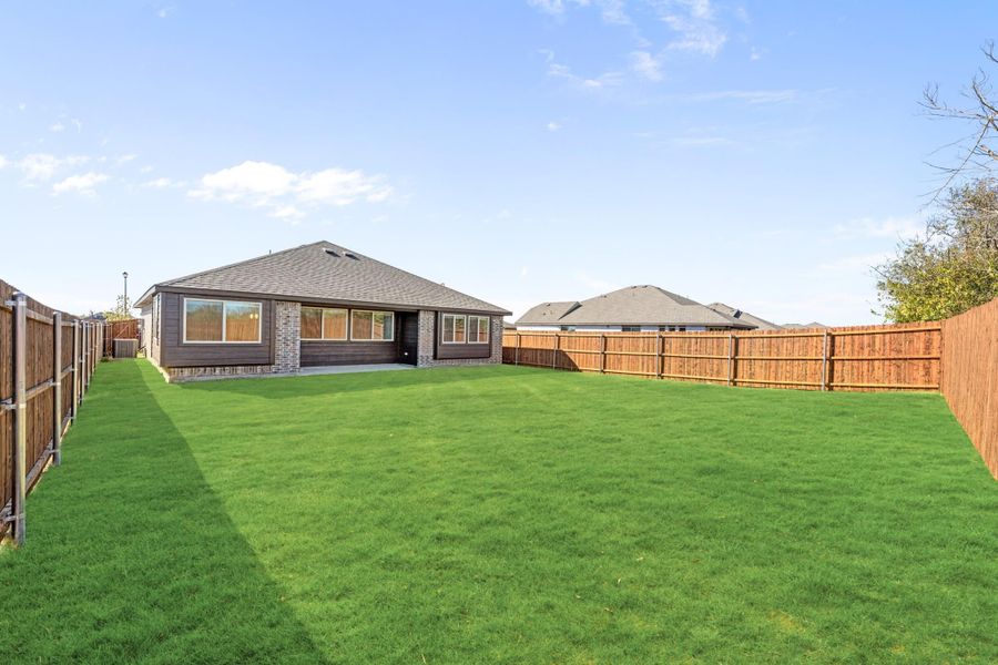 Large backyard with green lawn, wood privacy fence, and single-story brick home with large windows
