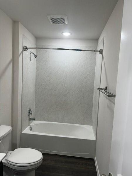 Full bathroom featuring vanity, hardwood / wood-style flooring, tiled shower / bath combo, and toilet