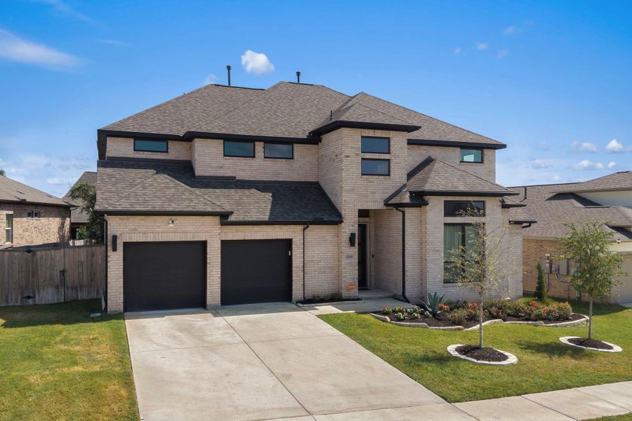 A striking contemporary residence boasts a light brick facade, dark garage doors, and meticulously landscaped grounds with mature trees. A striking contemporary residence boasts a light brick facade, dark garage doors, and meticulously landscaped grounds with mature trees.