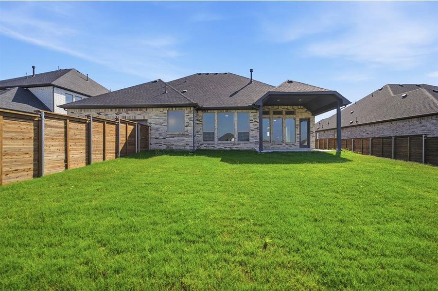 Expansive green lawn with a covered patio, full privacy fencing, and a brick and stone exterior
