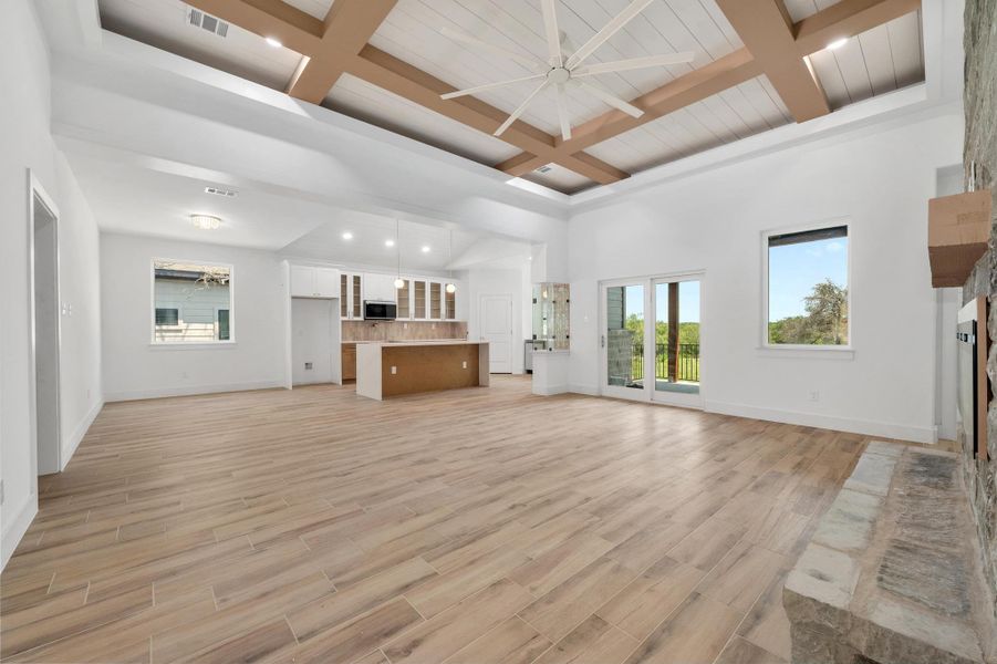 Living room with a large fireplace, coffered ceiling, light wood finished floors, beamed ceiling, and a ceiling fan Living room with a large fireplace, coffered ceiling, light wood finished floors, beamed ceiling, and a ceiling fan