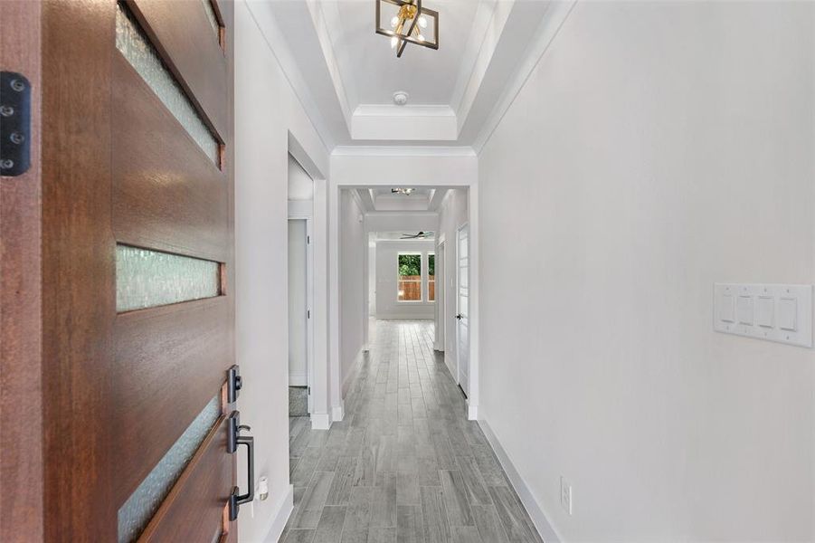 Hallway with crown molding, a raised ceiling, a notable chandelier, and hardwood / wood-style flooring