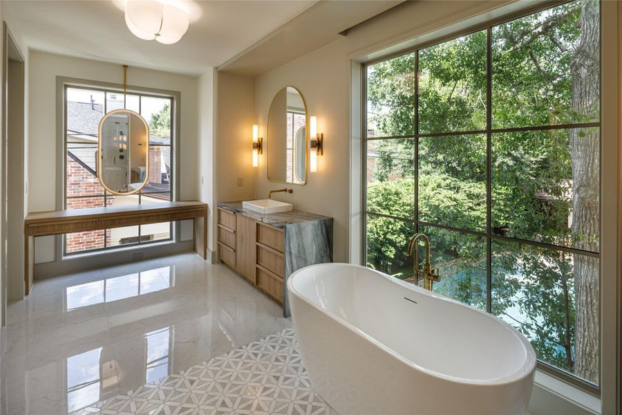 Possibly the best seat in the house. The freestanding tub overlooks the trees and pool through an enormous window, while custom cabinetry, stone, and warm brass keep the room feeling polished rather than precious.