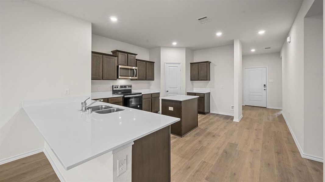 Kitchen featuring stainless steel appliances, a kitchen island, a peninsula, dark wood finish cabinets, and recessed lighting