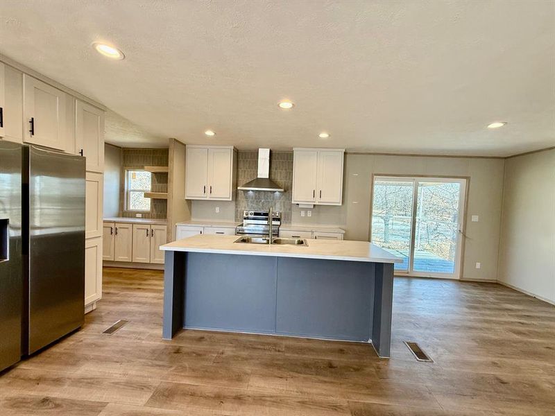 Dual tone kitchen featuring stainless steel appliances, open shelves, light wood-style floors, a kitchen island with sink, and two tone cabinetry Dual tone kitchen featuring stainless steel appliances, open shelves, light wood-style floors, a kitchen island with sink, and two tone cabinetry
