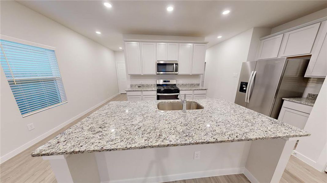 This photo showcases a modern kitchen with sleek granite countertops, stainless steel appliances, and ample cabinet space. The open layout and recessed lighting create a bright, welcoming atmosphere. and a huge kitchen island to accommodate three bar stools