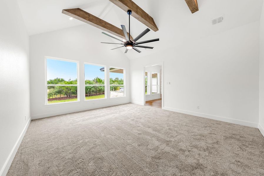 A spacious room features vaulted ceilings with exposed wood beams and broad windows offering abundant natural light.