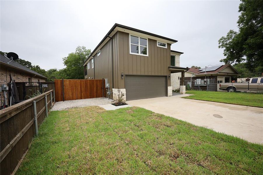 View of front of house featuring board and batten siding, concrete driveway, a garage, a gate, and stone siding