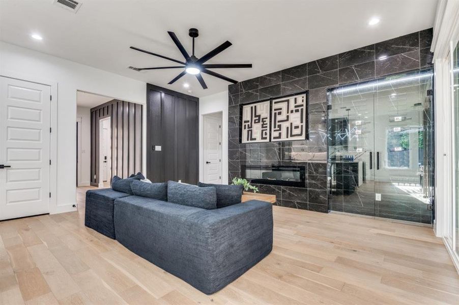 Living area featuring light wood-style floors, a fireplace, ceiling fan, tile walls, and recessed lighting Living area featuring light wood-style floors, a fireplace, ceiling fan, tile walls, and recessed lighting