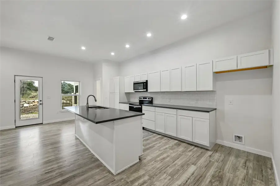 Kitchen featuring dark countertops, white cabinets, appliances with stainless steel finishes, recessed lighting, and a kitchen island with sink