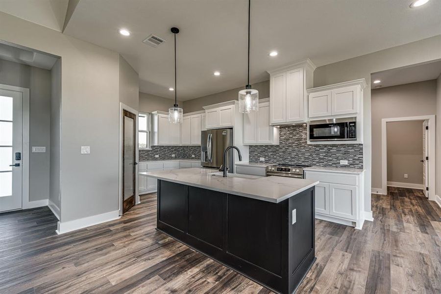 Kitchen with dark wood-type flooring, decorative light fixtures, sink, white cabinets, and appliances with stainless steel finishes