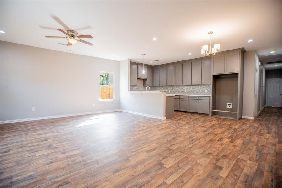 Unfurnished living room with wood-type flooring and ceiling fan with notable chandelier