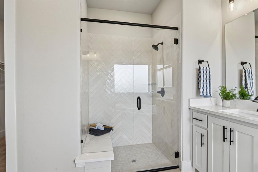 Walk-in shower with herringbone tile walls, glass door, built-in bench, and white vanity with black hardware nearby Walk-in shower with herringbone tile walls, glass door, built-in bench, and white vanity with black hardware nearby