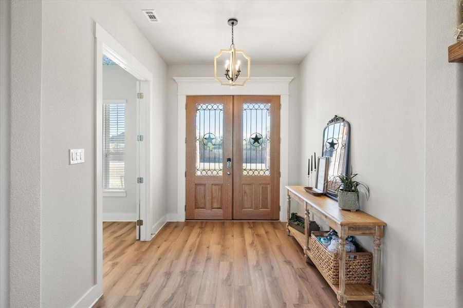 Foyer entrance with light wood-style floors, a chandelier, and a textured wall