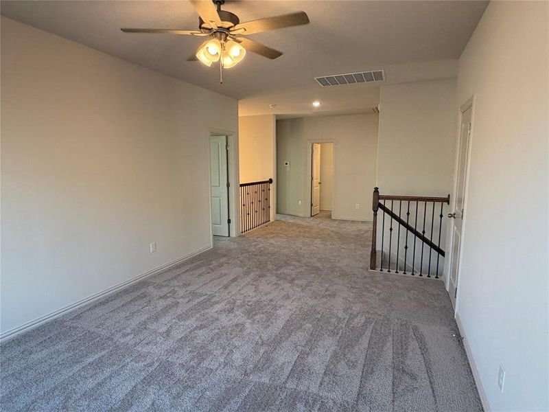 Spacious carpeted room featuring a ceiling fan with light fixture, light neutral wall paint, and white baseboards Spacious carpeted room featuring a ceiling fan with light fixture, light neutral wall paint, and white baseboards