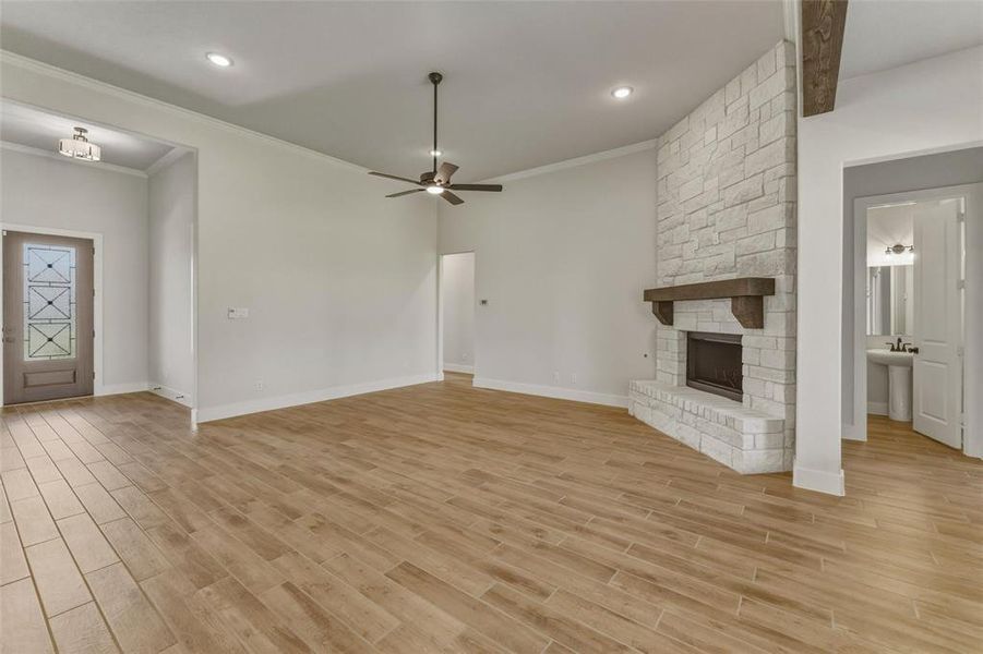 Spacious living area featuring wood-finish flooring, a stone fireplace with a wood mantel, and crown molding Spacious living area featuring wood-finish flooring, a stone fireplace with a wood mantel, and crown molding
