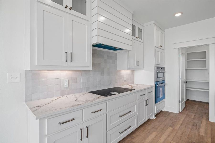 Modern kitchen featuring white shaker cabinetry, stone-finish countertops, tile backsplash, and a built-in wall oven and microwave