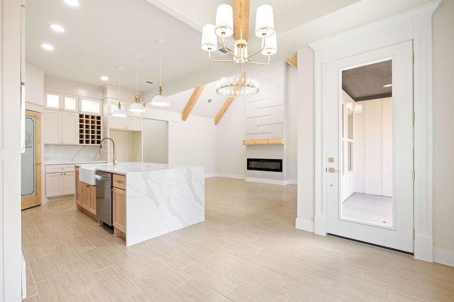 Kitchen featuring a center island with sink, a large fireplace, a sink, light stone countertops, and a chandelier