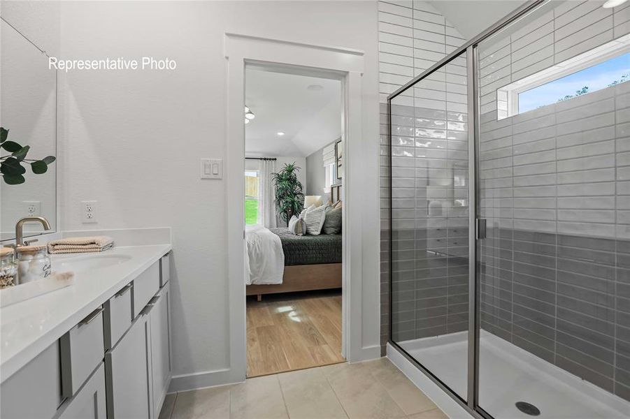 Bathroom featuring a glass-enclosed shower with tile surround, a linear window, a single vanity with a solid surface countertop, and light wood-finish flooring in the background Bathroom featuring a glass-enclosed shower with tile surround, a linear window, a single vanity with a solid surface countertop, and light wood-finish flooring in the background