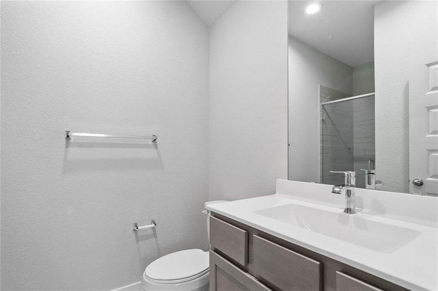 This secondary bath features tile flooring, shower with tile surround, stained wood cabinets, beautiful light countertops, mirror, sleek fixtures and modern finishes.