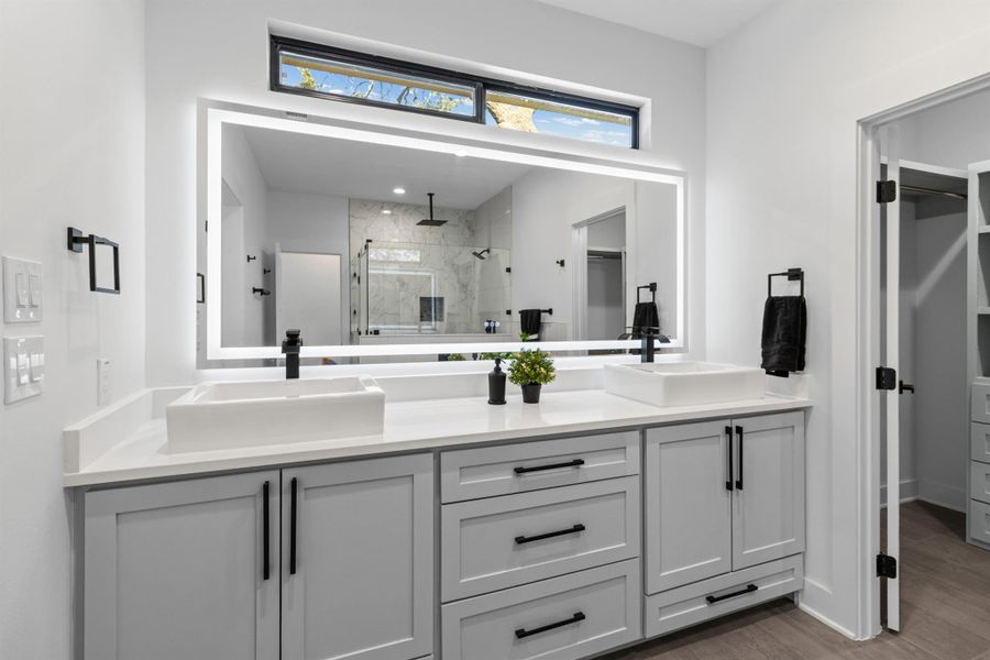 Full bath featuring a spacious closet, double vanity, a marble finish shower, and light wood-style floors