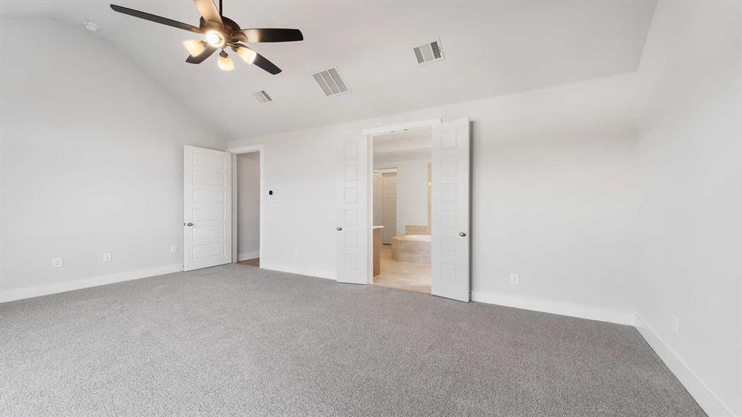 Unfurnished bedroom featuring lofted ceiling, connected bathroom, light carpet, and ceiling fan