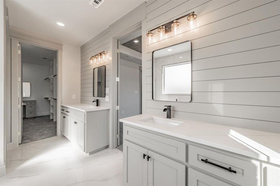 Full bathroom featuring two vanities, wooden walls, light marble finish floors, and recessed lighting