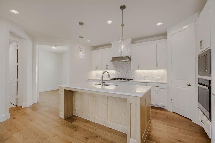 Contemporary kitchen featuring a central island with a sink, white cabinetry, integrated stainless steel appliances, and wood-finish flooring
