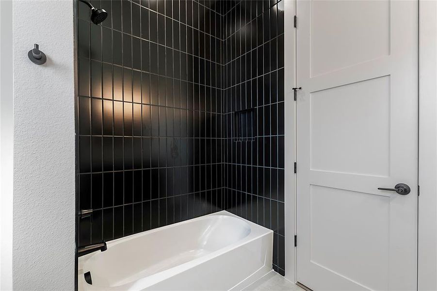 Bathroom featuring a white tub with dark hardware, black subway tile surround, and a built-in shower niche Bathroom featuring a white tub with dark hardware, black subway tile surround, and a built-in shower niche