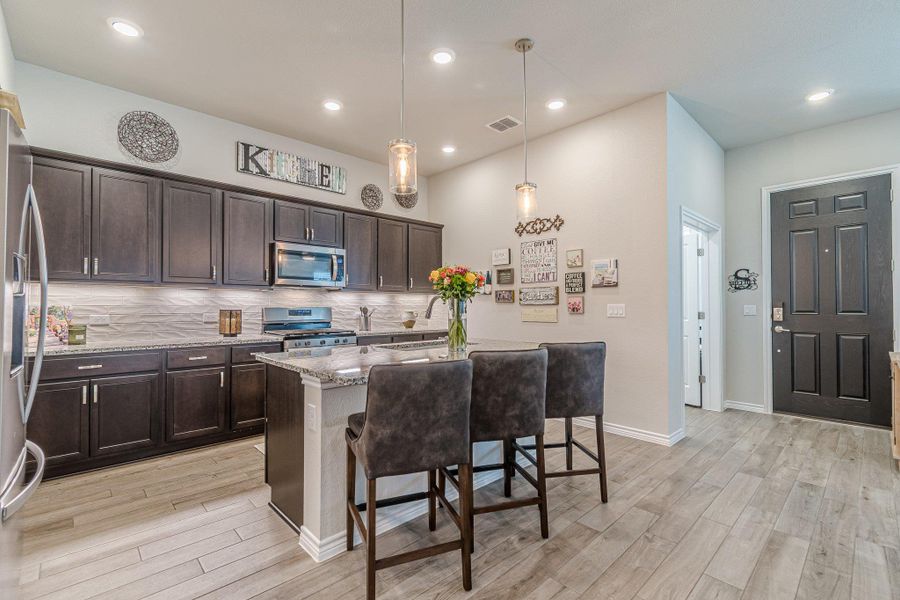 Kitchen featuring stainless steel appliances, light wood-style flooring, light stone countertops, dark brown cabinetry, and a breakfast bar area