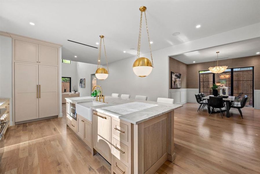 The property features light-toned hardwood flooring throughout, a kitchen island with a white farmhouse sink and gold-toned faucet, and statement gold and white pendant lighting