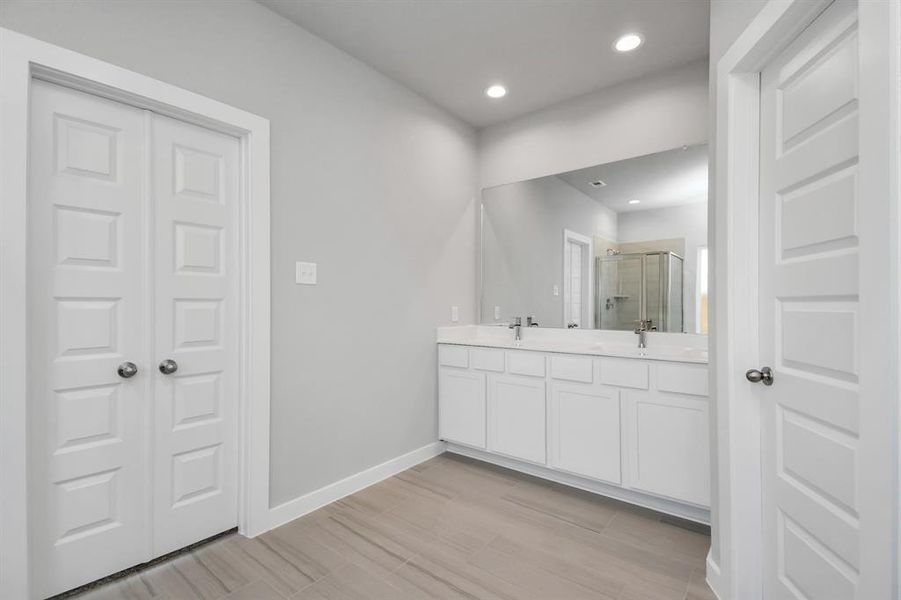 The expansive walk-in shower surrounded with tile and the distinct garden tub adorned with unique details will enhance your daily rituals at the sophisticated vanity, featuring double sinks, light-colored countertops, contemporary hardware, and exquisite vanity lights.  Sample photo of completed home with similar plan. As built color and selections may vary.