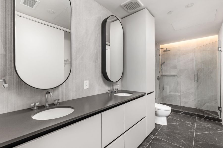 A well-appointed bathroom offers a dual vanity, sleek dark countertops, and a glass-enclosed shower.