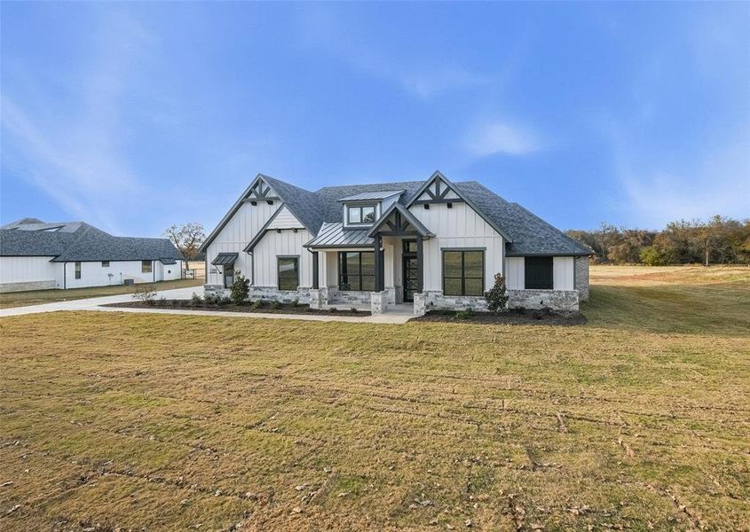 Modern farmhouse style home with a front yard, board and batten siding, a standing seam roof, and a metal roof Modern farmhouse style home with a front yard, board and batten siding, a standing seam roof, and a metal roof