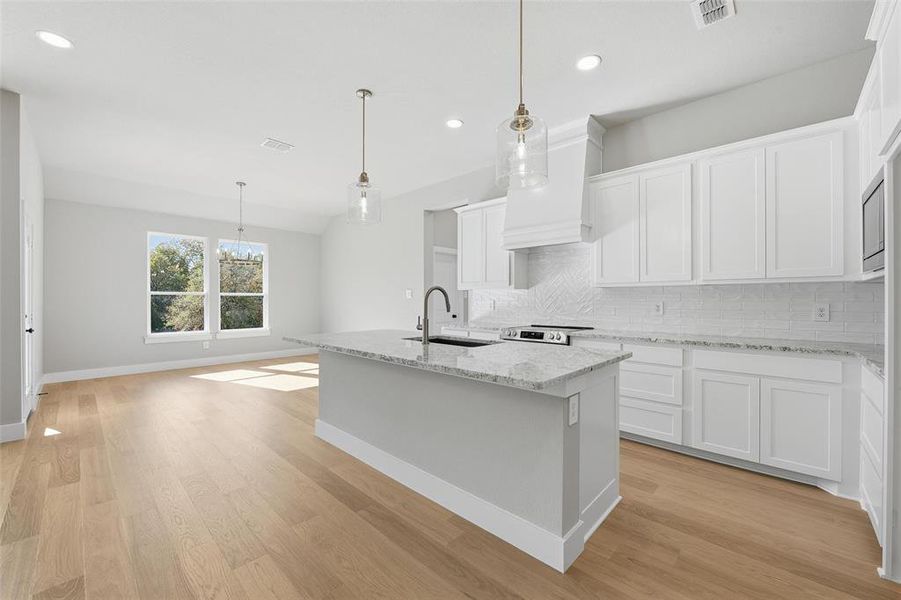 Kitchen with an island with sink, light stone countertops, white cabinets, decorative light fixtures, and light wood-style flooring Kitchen with an island with sink, light stone countertops, white cabinets, decorative light fixtures, and light wood-style flooring