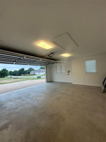Spacious garage featuring a concrete floor, overhead lighting, and an automatic garage door opener