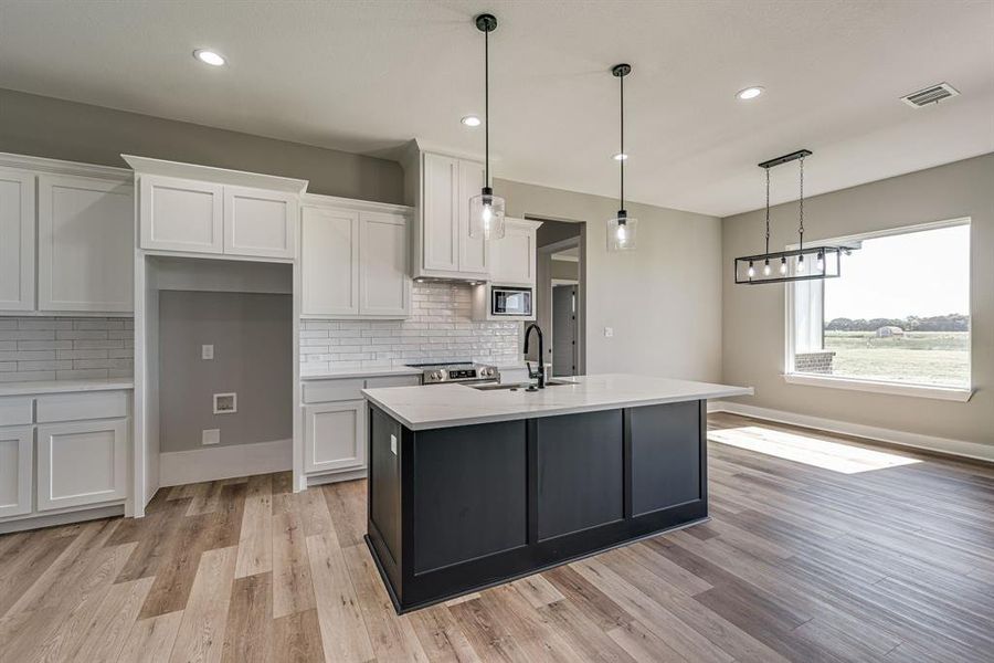 Kitchen featuring an island with sink, light wood-type flooring, white cabinetry, and sink