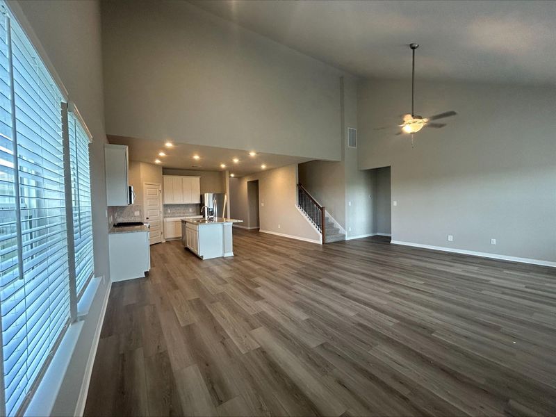 Unfurnished living room featuring high vaulted ceiling, plenty of natural light, stairs, a ceiling fan, and dark wood-type flooring Unfurnished living room featuring high vaulted ceiling, plenty of natural light, stairs, a ceiling fan, and dark wood-type flooring
