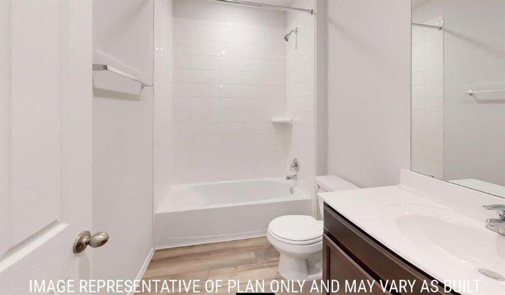 Bathroom featuring a white subway tile shower surround, integrated bathtub, dark wood-finish vanity with white countertop, and wood-finish flooring Bathroom featuring a white subway tile shower surround, integrated bathtub, dark wood-finish vanity with white countertop, and wood-finish flooring