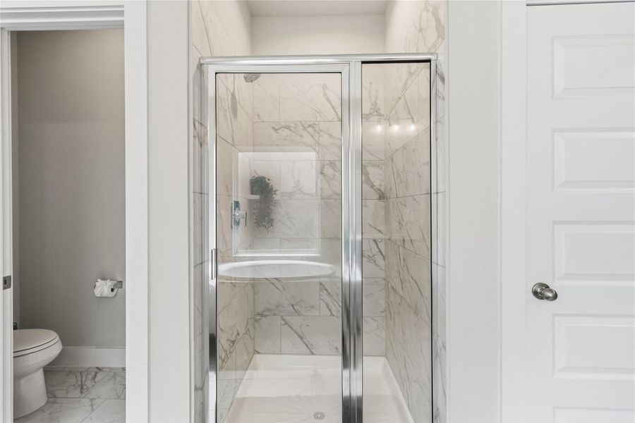 Your luxurious primary bath features a beautifully tiled walk-in shower with elegant marble-look surrounds, glass enclosure, and built-in niche for a true spa experience.