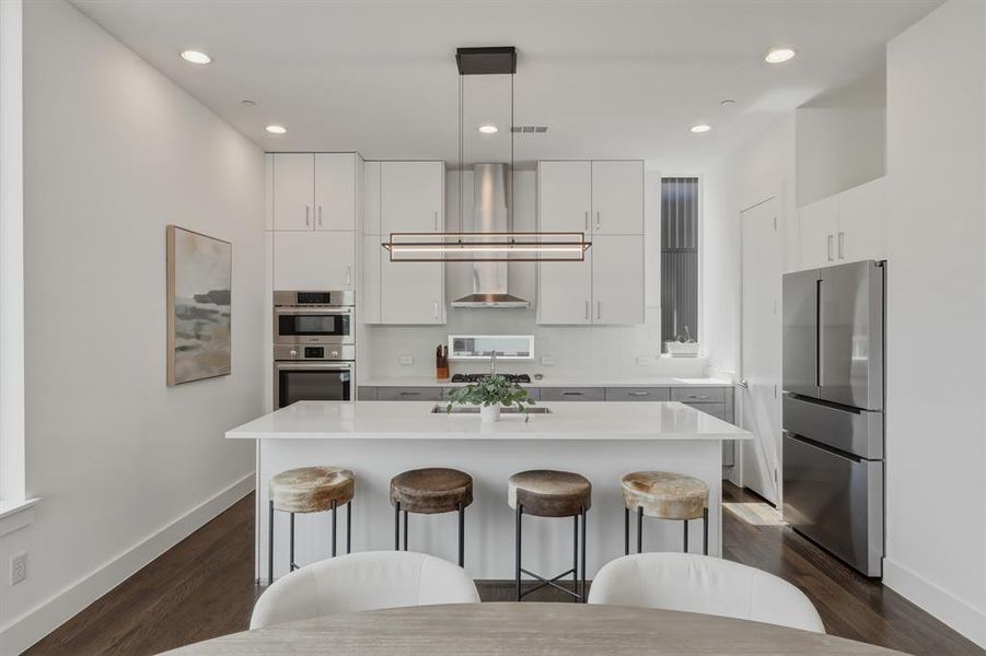 The kitchen features an island with a light-colored countertop, recessed lighting, and dark hardwood flooring