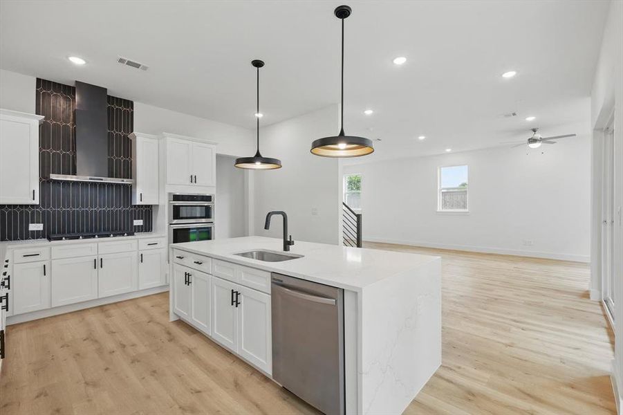 Kitchen with stainless steel appliances, a sink, wall chimney range hood, light wood-type flooring, and recessed lighting