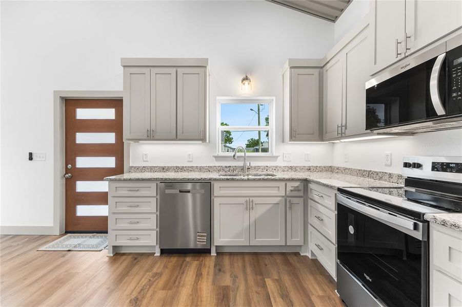 Kitchen with stainless steel appliances, a sink, wood finished floors, and light stone countertops Kitchen with stainless steel appliances, a sink, wood finished floors, and light stone countertops