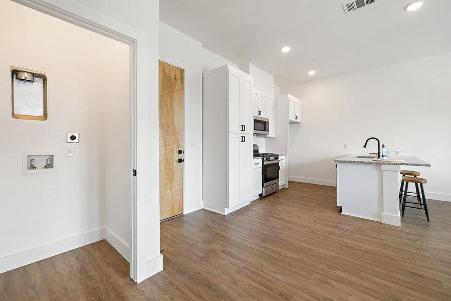 Kitchen with a breakfast bar, dark wood-style flooring, stainless steel appliances, white cabinetry, and recessed lighting