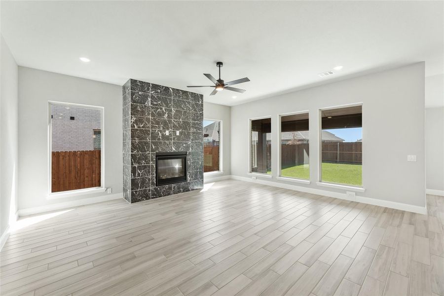 Open living room with dark marble tile fireplace, light wood floors, ceiling fan, and large backyard windows Open living room with dark marble tile fireplace, light wood floors, ceiling fan, and large backyard windows