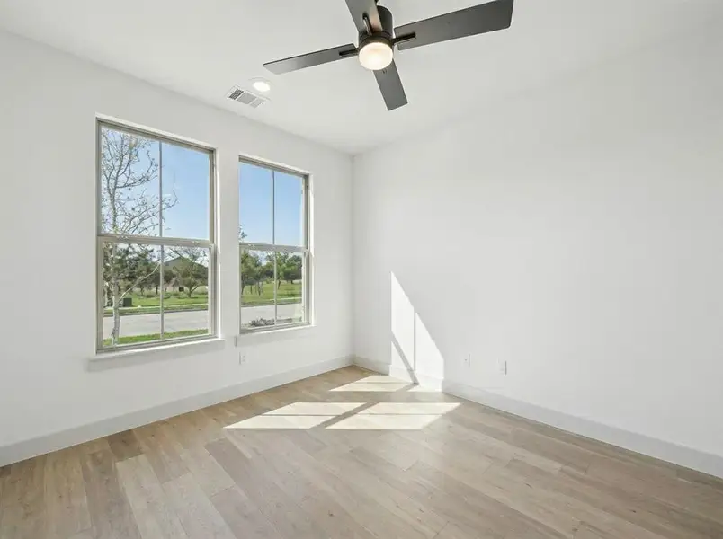 Bright interior space featuring two large windows, wood-finish flooring, a ceiling fan with integrated lighting, and recessed overhead lighting