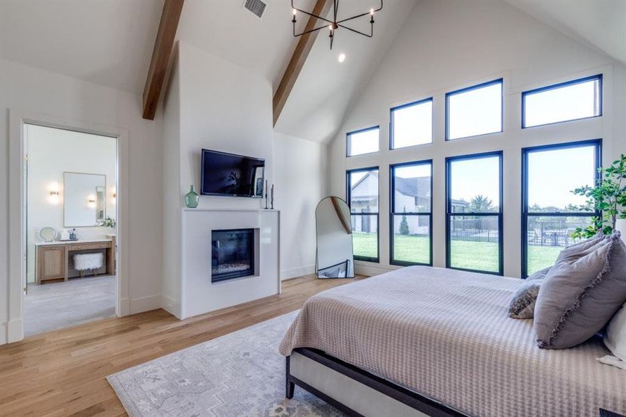 Bedroom with high vaulted ceiling, a glass covered fireplace, a chandelier, light wood-type flooring, and beam ceiling Bedroom with high vaulted ceiling, a glass covered fireplace, a chandelier, light wood-type flooring, and beam ceiling