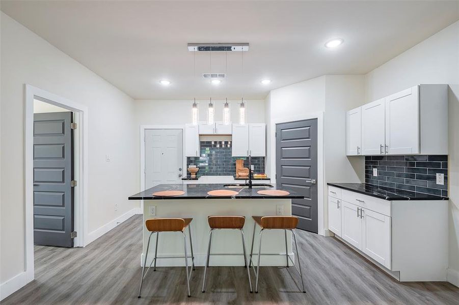 Kitchen featuring light hardwood / wood-style floors, tasteful backsplash, a center island with sink, and white cabinets